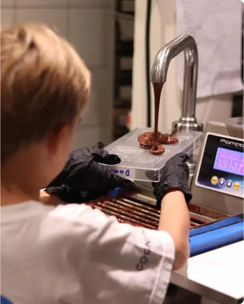 Chocolatier pouring melted chocolate into molds in a chocolate workshop