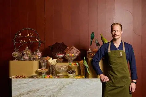 Chef Arne Riehn in green apron standing beside a chocolate and dessert display